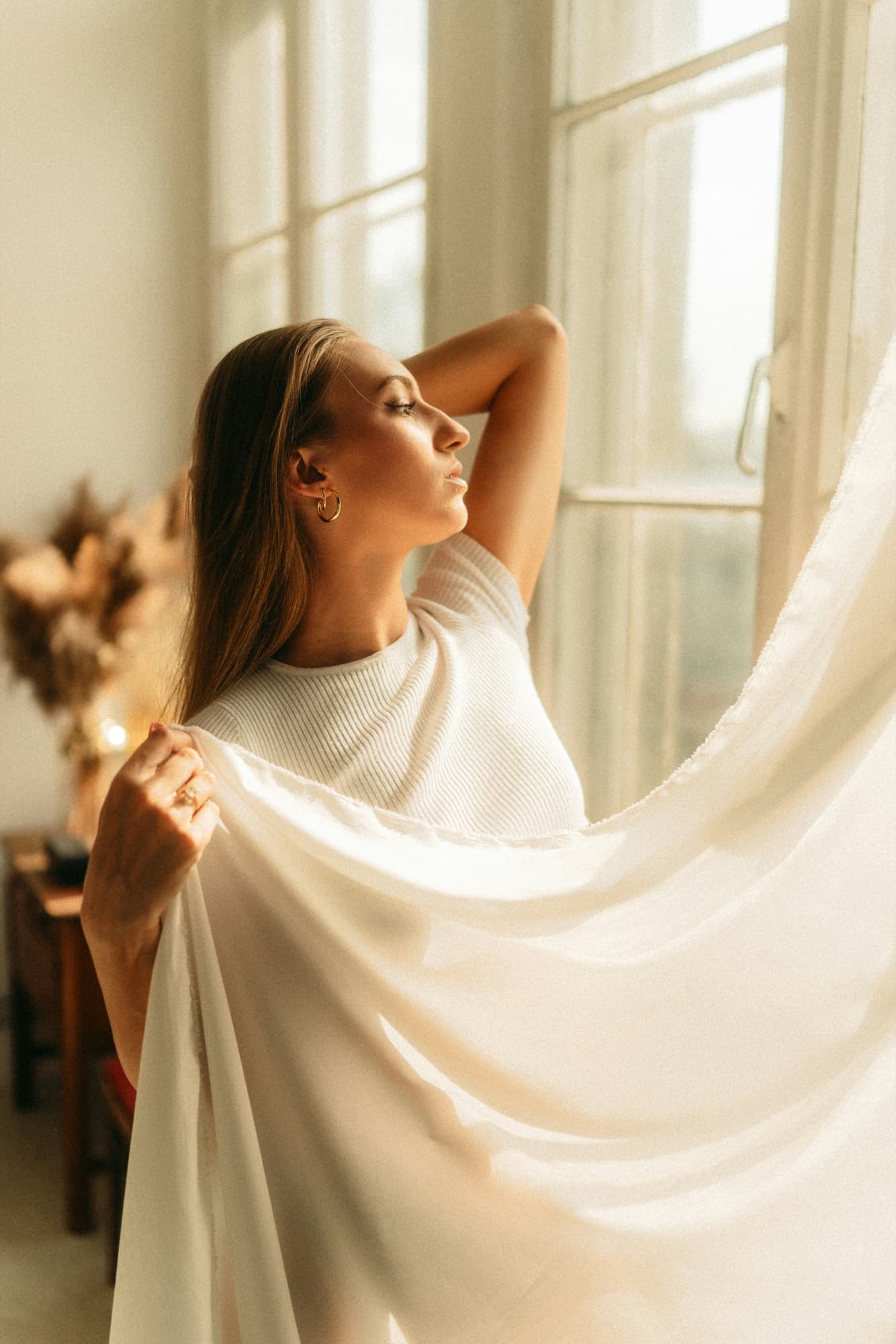 A woman standing in morning light beside an open window